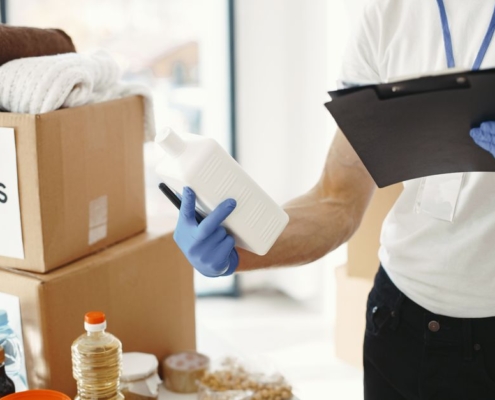 Diverse group of volunteers works together in a brightly lit space, sorting through boxes of food, water, and clothing don...