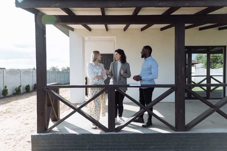 A group of diverse neighbors gathered on a sunny front porch, talking and laughing together, representing a strong, connected local community.