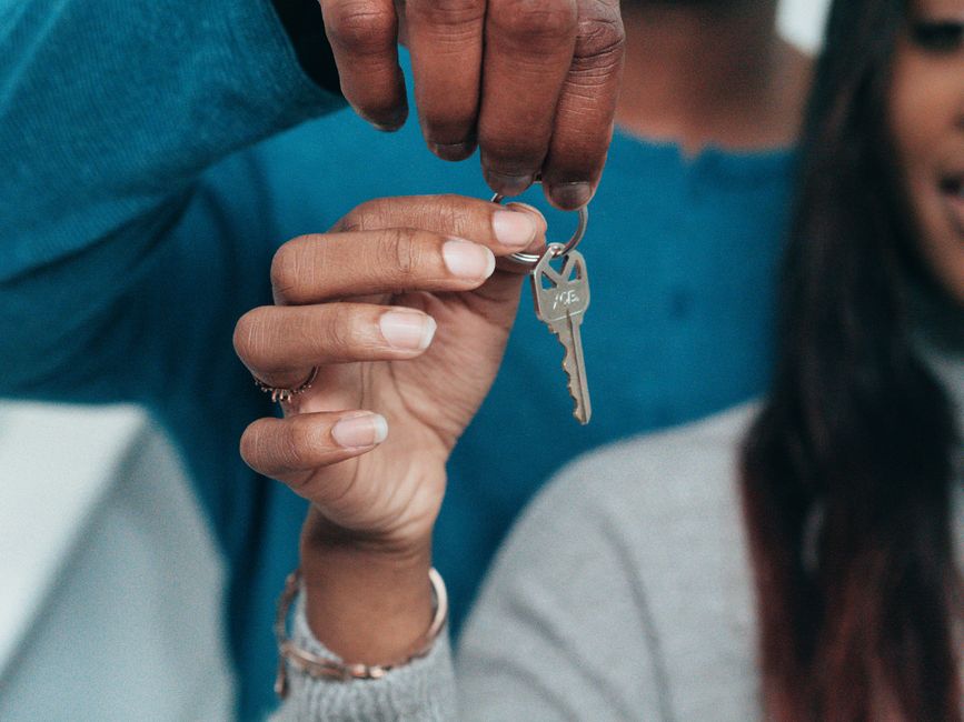 A happy, professional couple sits at a modern table, smiling as they review paperwork next to a set of new house keys, symbolizing financial wellness in real estate.