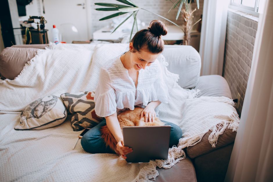 A person sits comfortably in a bright, modern living room, using a tablet to manage their real estate transaction, representing new low-commission models.